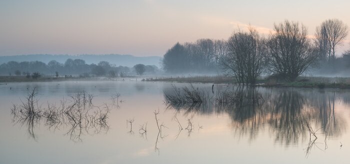 Fotobehang Landscape of lake in mist with sun glow at sunrise