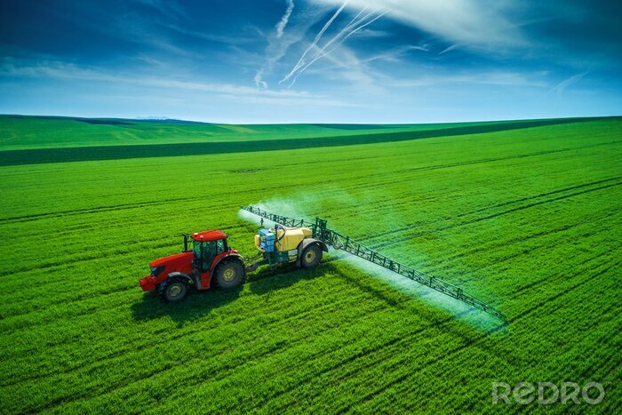 Fotobehang Luchtmening van de landbouw van tractor die en op gebied ploegt bespuit