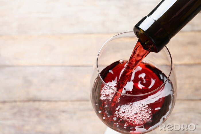Fotobehang Pouring red wine from bottle into glass on blurred background, closeup. Space for text