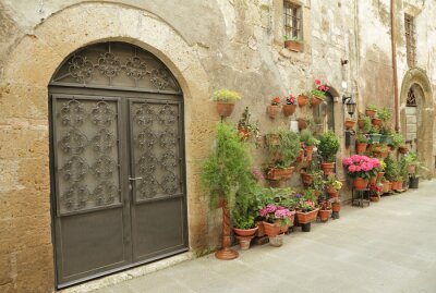 Fotobehang smeedijzeren hek en veel bloemen in Toscaanse dorp