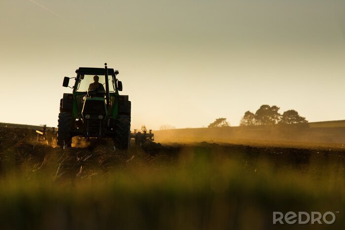 Fotobehang Tractor in een veld bij zonsondergang