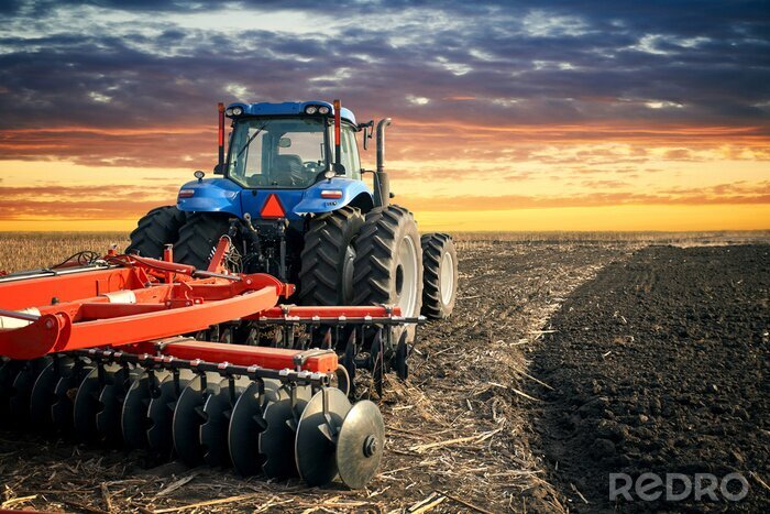 Fotobehang Tractor ploegend gebied op zonsondergangachtergrond