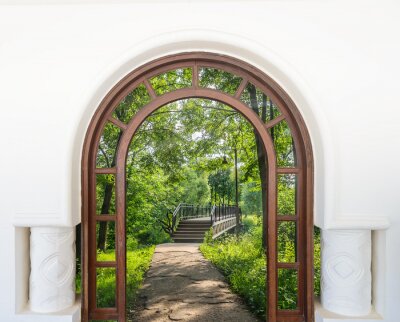 Fotobehang Uitzicht door de boogdeur op de brug en het groen