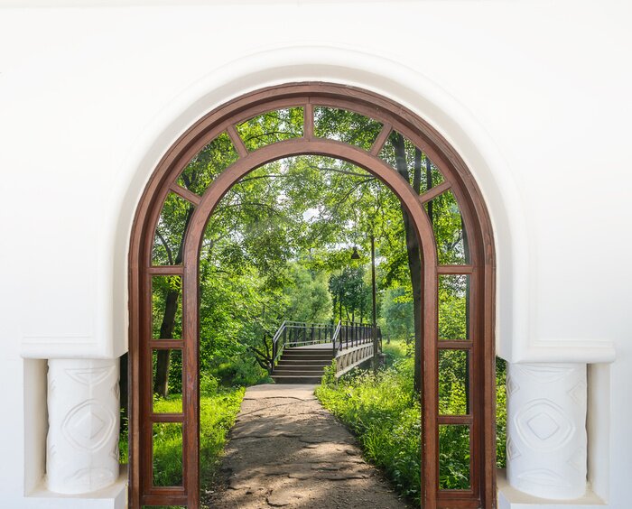 Fotobehang Uitzicht door de boogdeur op de brug en het groen
