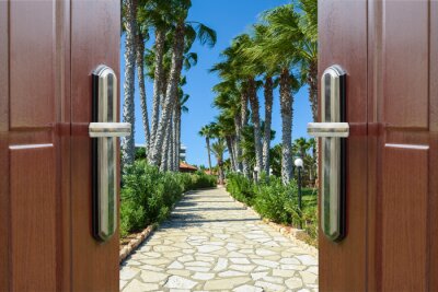 Fotobehang Uitzicht door de deur op het met palmbomen omzoomde trottoir