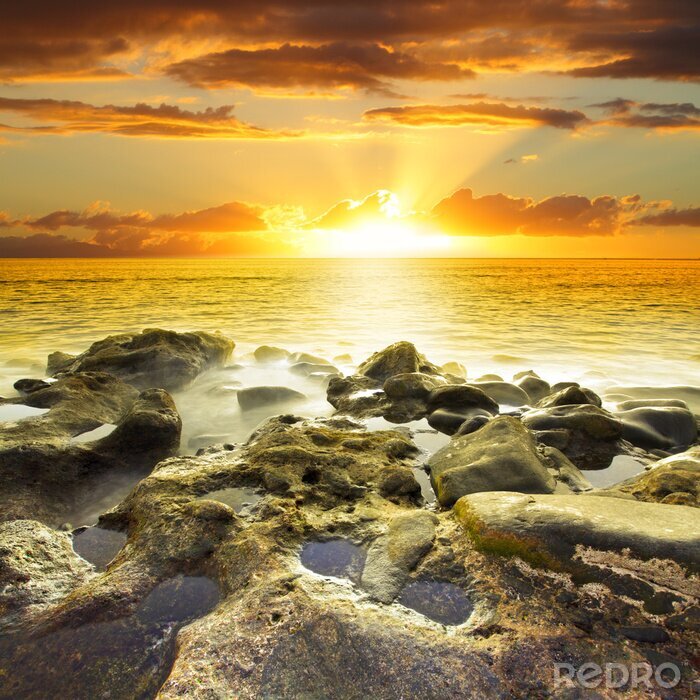 Fotobehang Verspreide stralen van de zon tegen de achtergrond van de zee
