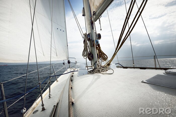 Fotobehang White yacht sailing on a sunny summer day. Close-up view from the deck to the bow, mast and sails. Waves and water splashes. Clear blue sky. Gulf of Finland