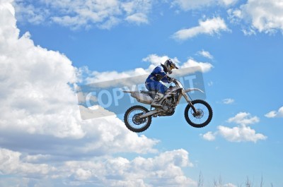 Fotobehang Motocross rider staan ​​op de motor MX vliegt over de heuvel op een achtergrond van blauwe hemel
