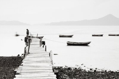 Fotobehang Zwart-witbeeld van een man op een pier en boten op het water