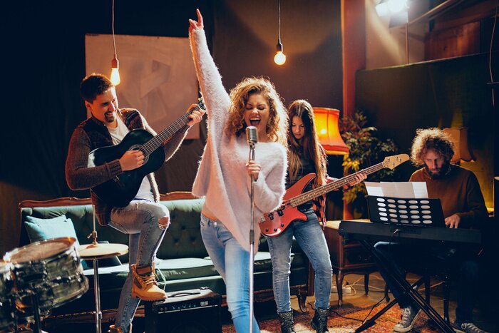 Poster Band practice for the show. Woman with curly hair holding microphone and singing while man in background playing acoustic guitar. Home studio interior.