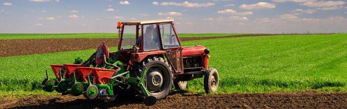 Poster Boer met tractor het zaaien op de akkers op zonnige sprin