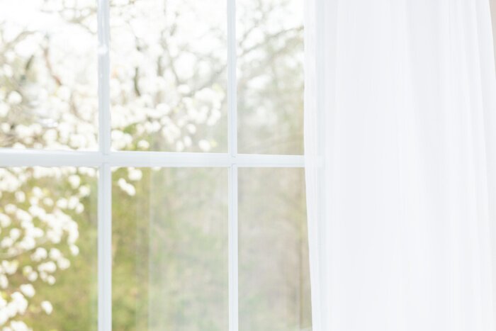 Poster Close-up van moderne witte kantgordijnen met mening door glasvenster op tuin in de lente of de zomer met sakura, de boom van kersenbloesembloemen