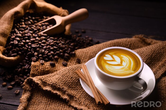 Poster Cup of coffee latte and coffee beans in burlap sack on old wooden background