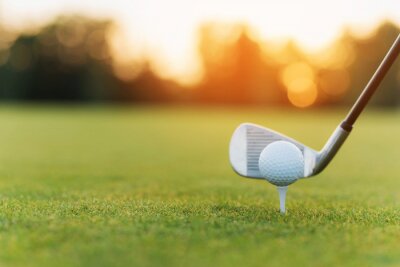 Poster De golfclub achter de golfbal op de tribune. Tegen de achtergrond van gras en zonsondergang