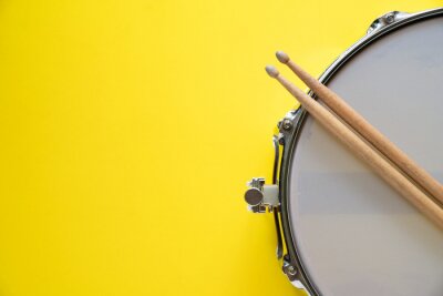 Poster Drum stick and drum on yellow table background, top view, music concept