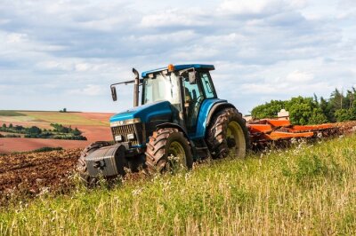 Poster Een blauwe tractor aan het werk op een veld op een heldere dag.