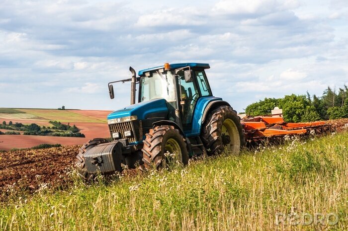Poster Een blauwe tractor aan het werk op een veld op een heldere dag.
