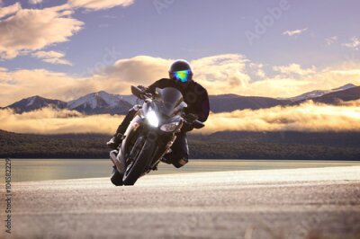 Poster Een motorrijder rijdt met bergen op de achtergrond, vermengd met wolken.