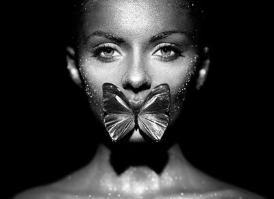 Poster Fashion model woman in bright sparkles and lights posing in studio. Portrait of beautiful sexy woman with butterfly. Art design glitter glowing make up. Black and white photography