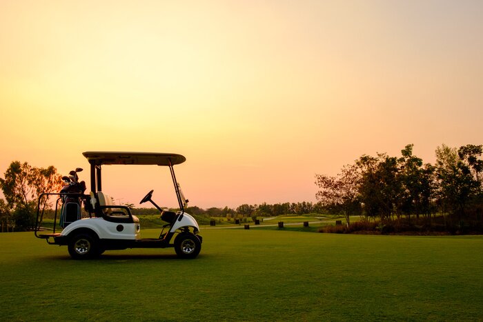 Poster Golf cart car in fairway of golf course with fresh green grass field and cloud sky and tree  on sunset time