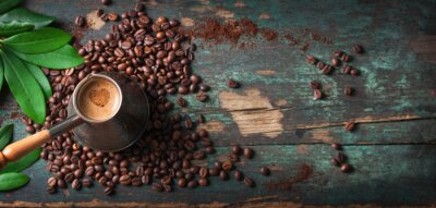 Hete koffie in een koffiekan of turk op een houten achtergrond met koffie bladeren en bonen, horizontale met kopie ruimte. bovenaanzicht