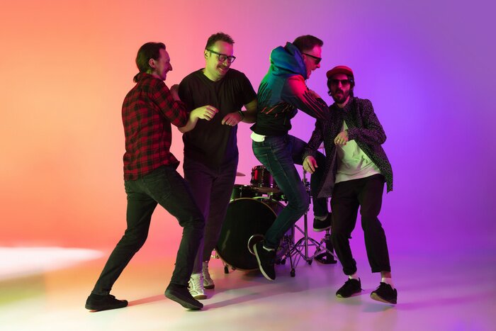 Poster High jump. Young inspired and expressive music band performing on gradient colored background in neon light. Concept of music, hobby, festival, art. Joyful artist, colorful, bright portrait.