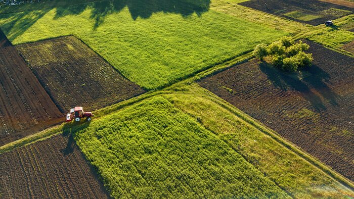 Poster Luchtmening van de hommel, een vogelperspectief van landbouwgebieden met een weg door en een tractor op het in de de lenteavond bij zonsondergang