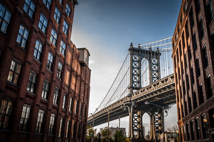 Poster Manhattan Bridge gezien vanuit een smal steegje omsloten door twee bakstenen gebouwen op een zonnige dag in de zomer