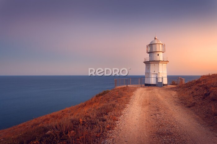 Poster Mooie witte vuurtoren op de oceaan kust bij zonsondergang. Lan