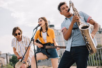 Poster Multiraciale jonge mensen met gitaar, djembe en saxofoon die op straat presteren