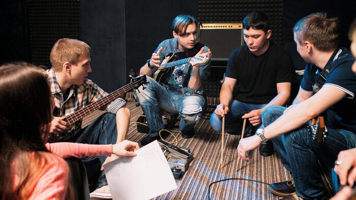 Poster Muziekband bespreken drummers partij in een lied. Vooraanzicht op jonge musici op de grond zitten, iedereen op zoek naar man met drumsticks.