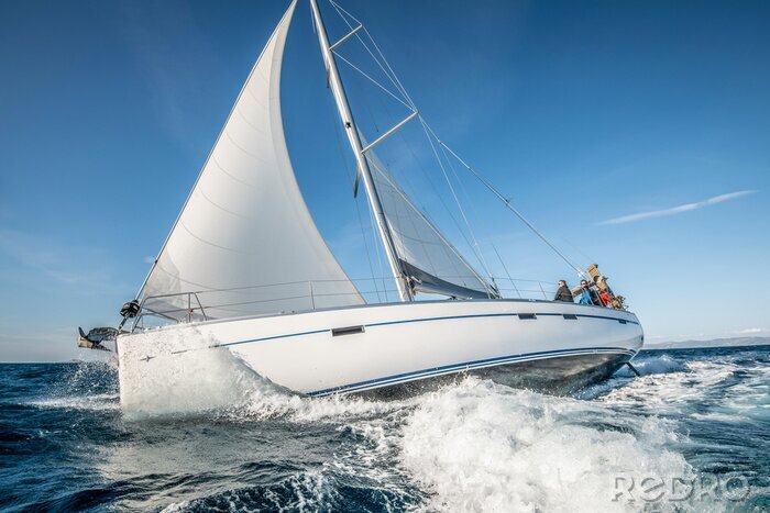 Poster One white sailing yacht floats on the sea with waves and spray. The view from the side