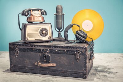 Poster Retro radio uit de jaren 60, oude koperen telefoon, studiomicrofoon uit de jaren 50 en goudkleurige vinylschijf opnemen circa 70s, koptelefoon op oude klassieke reiskoffer. Vintage stijl gefilterde fo