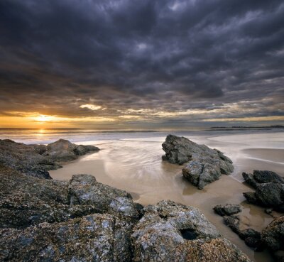 rotsen op strand bij zonsopgang met dramatische hemel