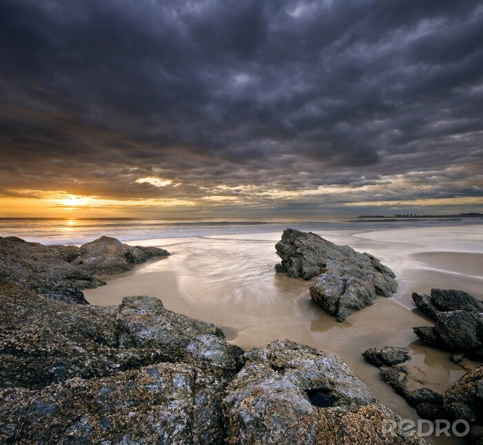 Poster rotsen op strand bij zonsopgang met dramatische hemel