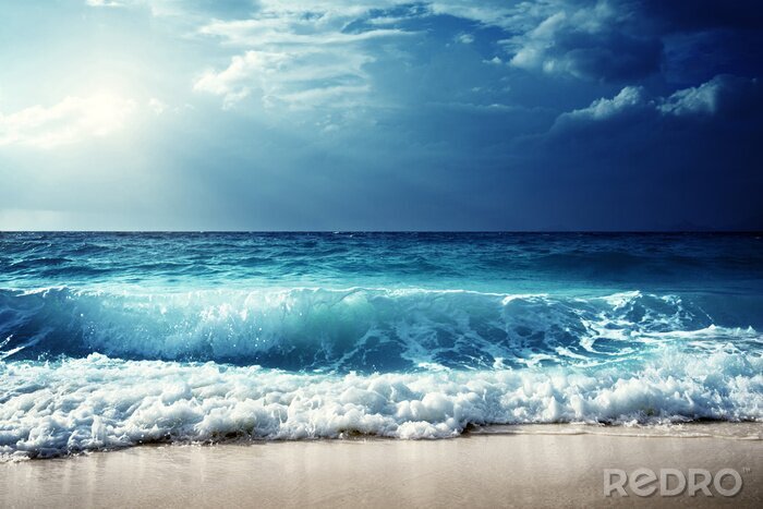 Poster Schuimende golven die tegen de kust van een zandstrand beuken
