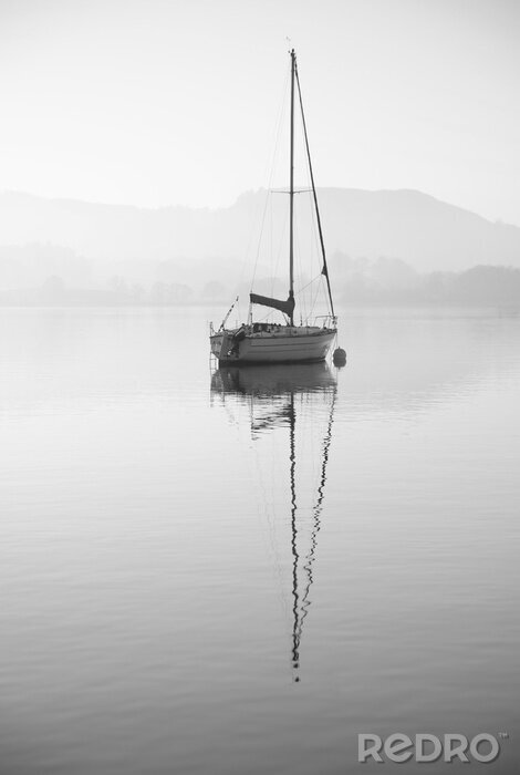 Poster Stunning unplugged fine art landscape image of sailing yacht sitting still in calm lake water in Lake District during peaceful misty Autumn Fall sunrise