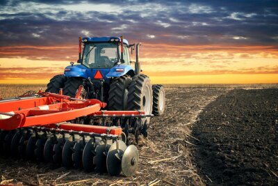 Tractor ploegend gebied op zonsondergangachtergrond