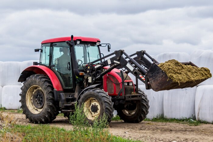 Poster Tractor with front end  loader scored feed for cows. View of the side on the background of bales with silage. Necessary equipment for a dairy farm.