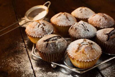 Vanille en chocolade muffins, basterdsuiker, zeef voor het bakken op een donkere houten achtergrond, selectieve aandacht