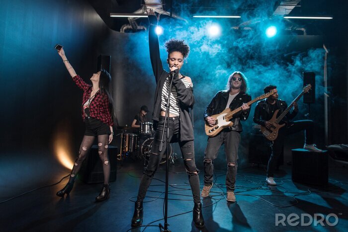 Poster Vrouwelijke zangeres met microfoon en rock-and-roll band die hard rockmuziek uitvoeren op het podium