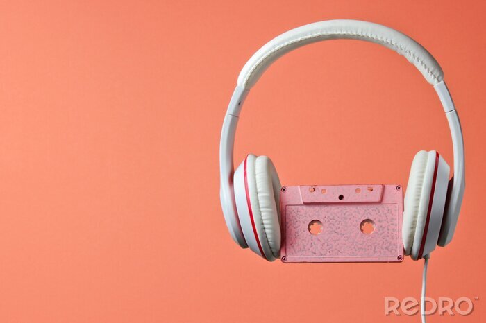 Poster White classic wired headphones with audio cassette isolated on coral color background. Retro style. 80s. Minimalistic music concept.
