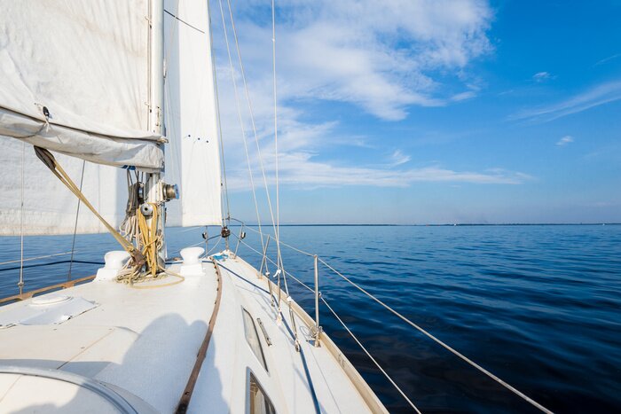 Poster White sloop rigged yacht sailing near the coast of Maine, Southwest Harbor, USA. A view from the deck to the bow, mast and sails. Dark blue storm sky, sun rays through the clouds
