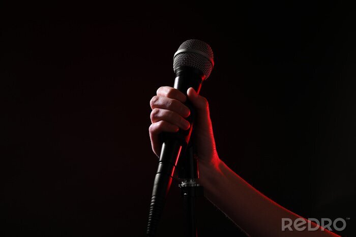 Poster Woman holding microphone on black background, closeup