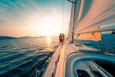 Poster Young couple enjoys sailing in the tropical sea at sunset on their yacht.